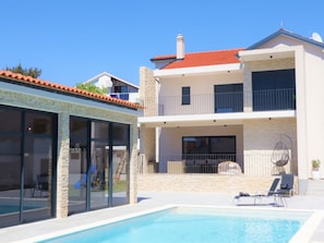 Ein modernes, zweistöckiges Haus mit Pool, Balkon und Terrasse.