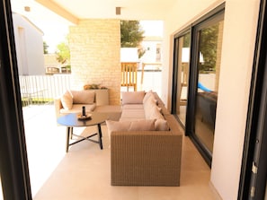 Eine sonnendurchflutete Terrasse mit einem Korbsessel, einem kleinen Tisch und einer Glastür, die auf einen Balkon führt.