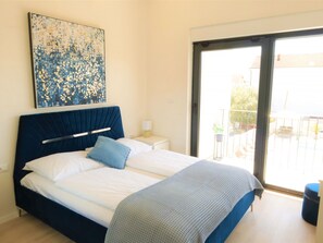 Un dormitorio con cama, mesita de noche, una obra de arte en la pared y puerta corrediza de vidrio que da a un área exterior.