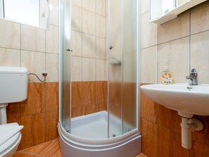 Un baño moderno con ducha envuelta en vidrio, un inodoro blanco y un lavamanos con una botella de jabón líquido.