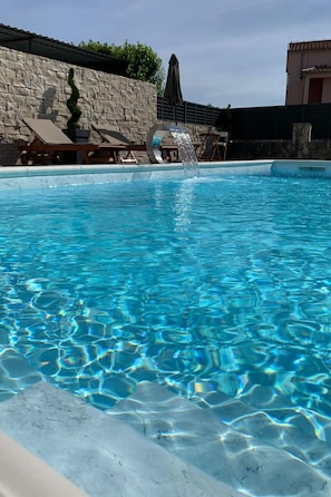 A swimming pool with clear blue water, lounge chairs, and a stone wall. - Apartment Julia A4, 2+2 by Interhome (Biograd na Moru)
