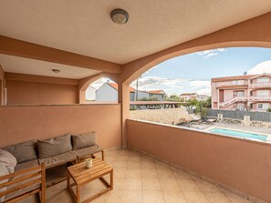 A balcony with a sofa, a small table, and a view of a swimming pool and buildings. - Apartment Julia A4, 2+2 by Interhome (Biograd na Moru)