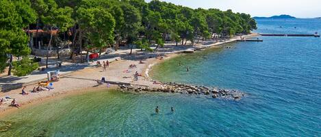 Una playa con agua cristalina, árboles y gente.