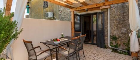 Um pátio externo com mesa, cadeiras, estrutura de pérgola e piso de pedra.