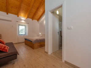 Ein Schlafzimmer mit Holzbalkendecke, einem Bett, einem Fenster und einer Badezimmertür.