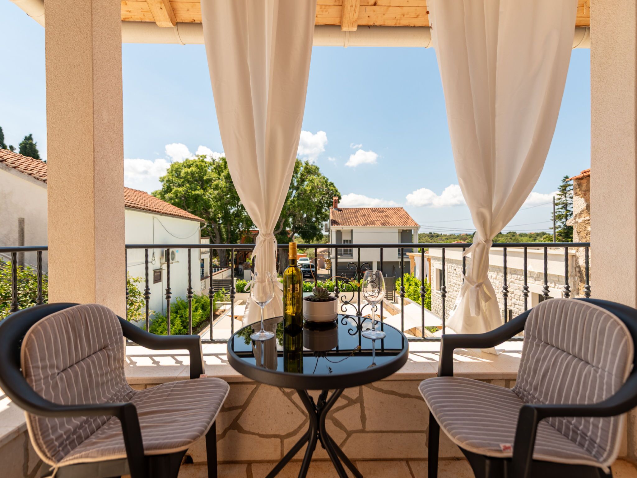 A balcony with two chairs, a table, and a bottle of wine.