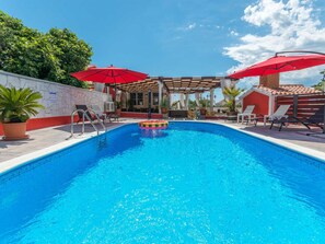 Ein Pool mit Sonnenschirm, Liegestühlen und einer Pergola.