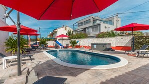 A swimming pool with red umbrellas, lounge chairs, and a stone wall. - Vacation home  by Interhome (Donje Rastane)
