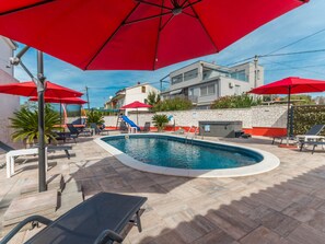 A swimming pool with red umbrellas, lounge chairs, and a stone wall. - Vacation home  by Interhome (Donje Rastane)