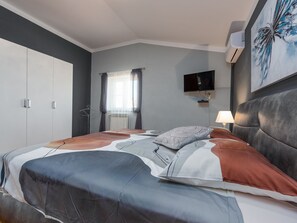 A bedroom with a bed, a TV mounted on the wall, and a painting above the bed. - Vacation home  by Interhome (Donje Rastane)