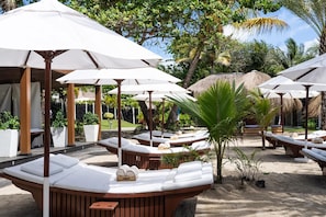 A resort with sun loungers under white umbrellas, surrounded by palm trees and a sandy beach. - Hilton Luxury Hotel – Rooms Only | Mandatory All-Inclusive Paid At Hotel (Dubai)