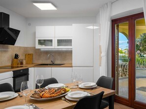 A modern kitchen with white cabinets, a wooden countertop, and a dining area with a table set for two. - Charming Villa Rea, 8+2 with heated pool by Interhome (Donje Rastane)