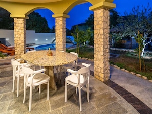 An outdoor patio with a round table and chairs, stone pillars, and a pool in the background. - Vacation home  by Interhome (Donje Rastane)