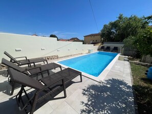 A rectangular swimming pool with a tiled deck, surrounded by a low white wall and a stone base. There are two lounge chairs and a small table with a glass top. - Vacation home  by Interhome (Donje Rastane)