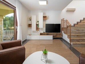 A modern living room with a flat-screen TV, a coffee table with a plant, and a staircase with wooden railings. - Vacation home  by Interhome (Donje Rastane)