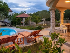 A pool area with lounge chairs, a stone pillar, and a small gazebo. - Vacation home  by Interhome (Donje Rastane)