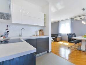 A modern kitchen with a built-in dishwasher, a grey sofa, and a dining table with chairs. - Apartment  by Interhome (Donje Rastane)