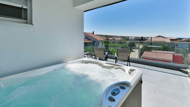Een balkon met een jacuzzi, stoelen en uitzicht op huizen.