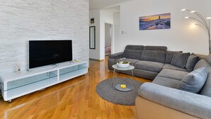 Een moderne woonkamer met een flatscreen televisie, een grijze bank en een schilderij aan de muur.