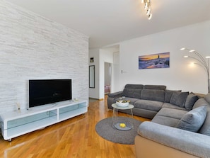 A modern living room with a flat-screen TV, grey sofa, and a painting on the wall. - Apartment  by Interhome (Donje Rastane)