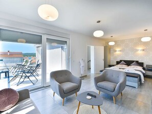 A modern hotel room with a balcony, two armchairs, a round coffee table, a bed with a headboard, and a large window. - Apartment  by Interhome (Donje Rastane)