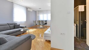 Een moderne woonkamer met een grijze bank, een eettafel met stoelen en een keukenhoek met een wasmachine.
