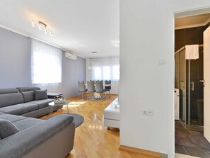 A modern living room with a grey sofa, a dining table with chairs, and a kitchen area with a washing machine. - Apartment  by Interhome (Donje Rastane)