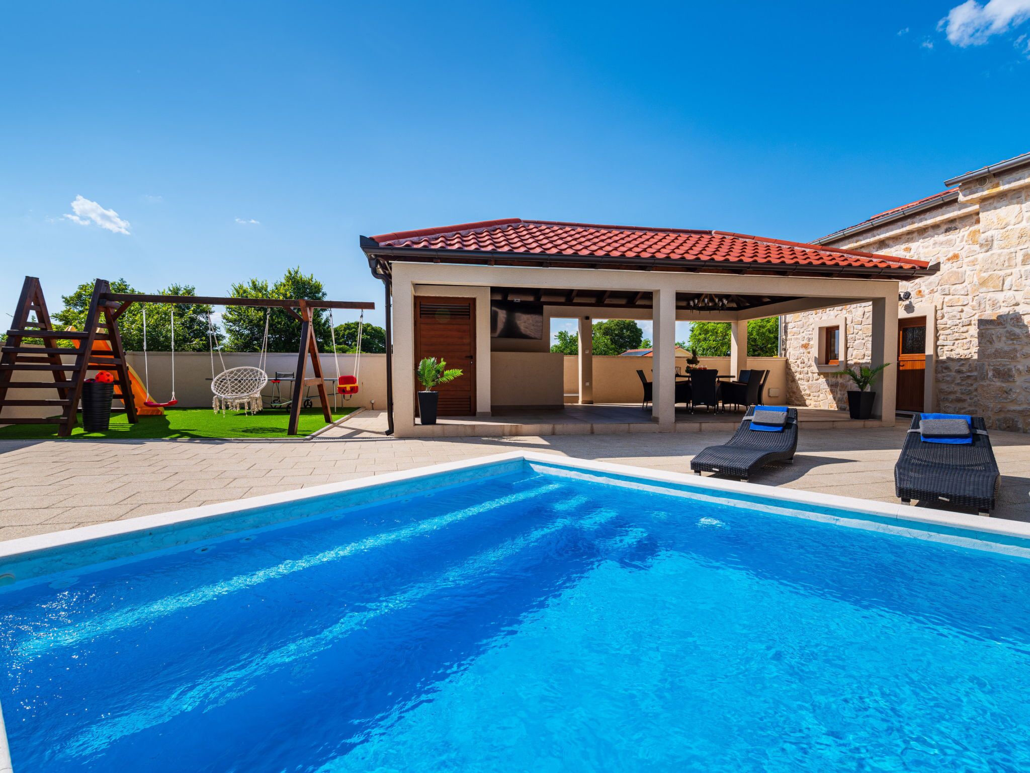 Ein Schwimmbecken mit Liegestühlen und einer überdachten Terrassenfläche.