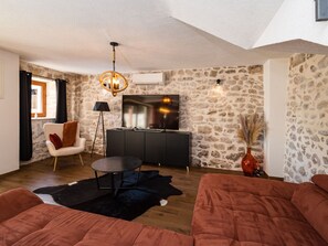 A modern living room with a stone wall, a flat-screen TV, a black sofa, a round coffee table, and a chandelier. - Villa Miandri with heated pool by Interhome (Debeljak)