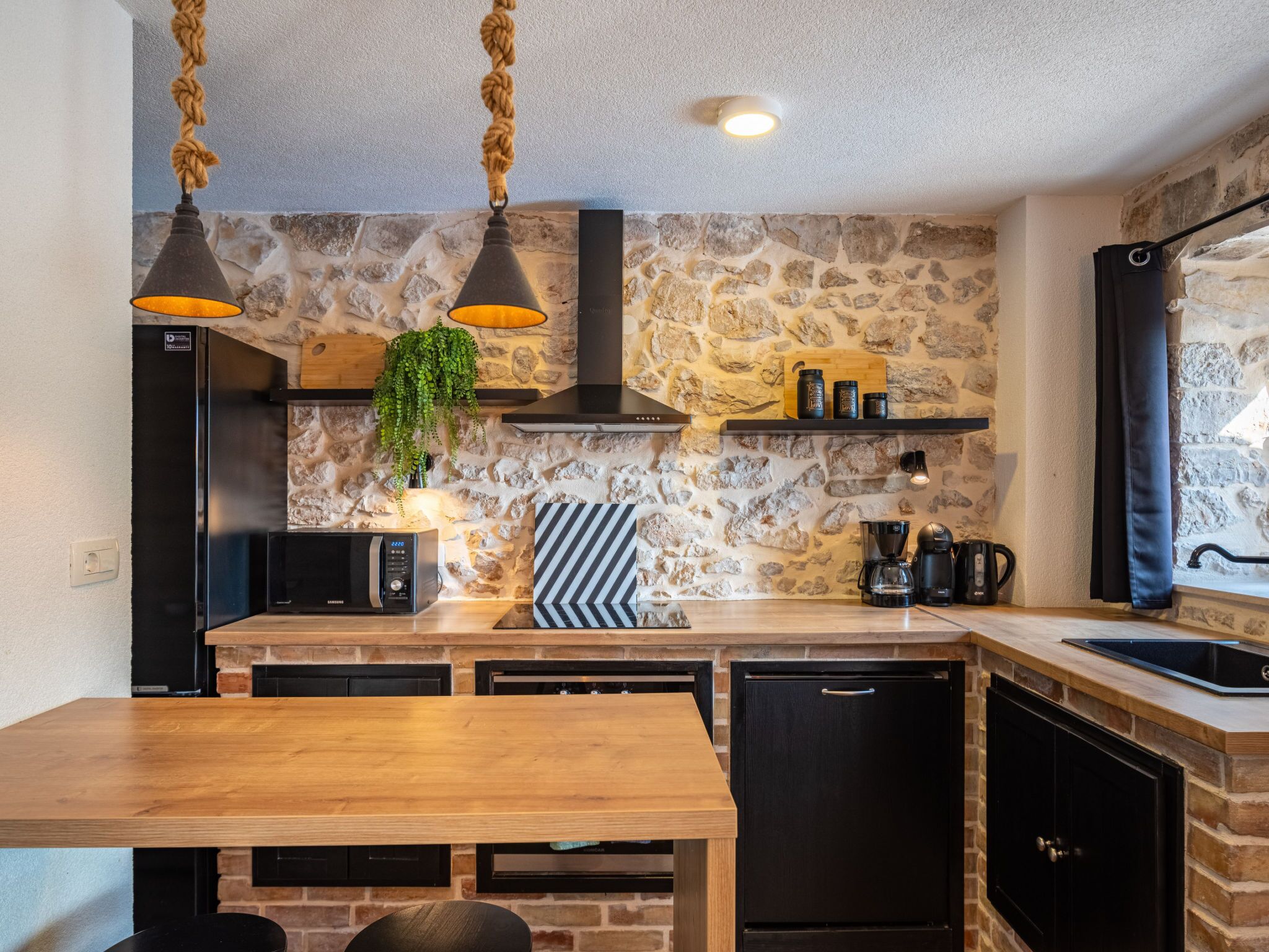 A kitchen with a stone wall, wooden countertop, and modern appliances.