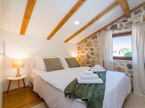 A bedroom with a stone wall, wooden beams, a bed with white linens, a green throw, and a bedside lamp. - Villa Miandri with heated pool by Interhome (Debeljak)