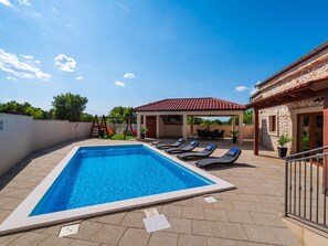 A rectangular swimming pool with lounge chairs, a covered patio area, and a stone building with a tiled roof. - Villa Miandri with heated pool by Interhome (Debeljak)