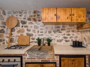 A kitchen with a stone wall, wooden cabinets, a gas stove, a wooden cutting board, and two potted plants. - Villa Miandri with heated pool by Interhome (Debeljak)