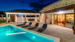 Ein Pool mit Liegestühlen, eine überdachte Sitzgruppe im Freien und ein Gebäude mit Glasüren.