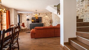A spacious living area with a stone wall, a sofa, a dining table with chairs, and a staircase.