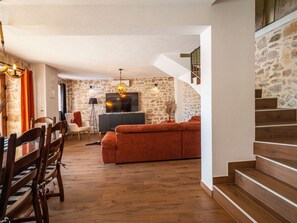 A spacious living area with a stone wall, a sofa, a dining table with chairs, and a staircase.