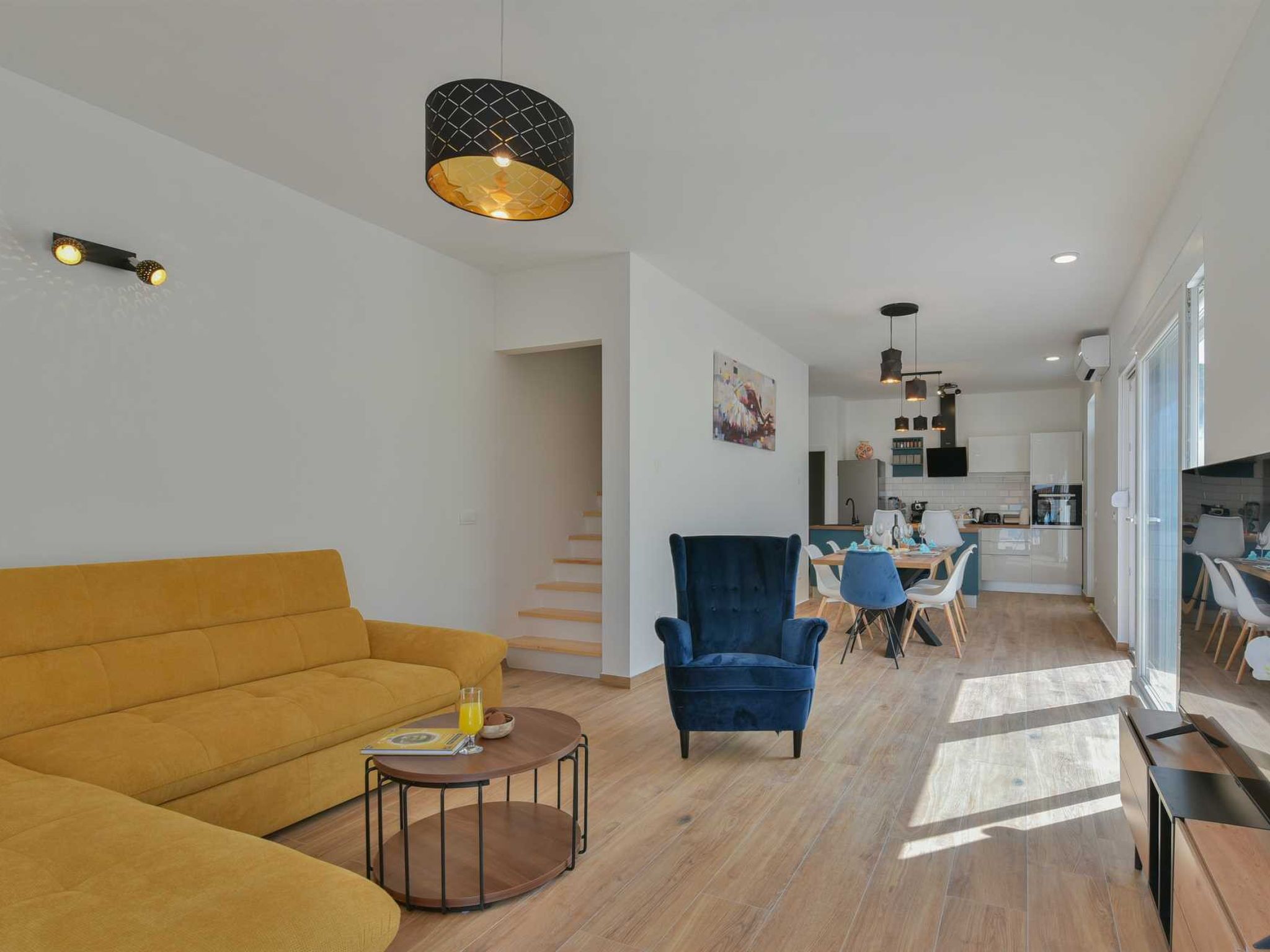 A modern living room with a sofa, a chair, a coffee table, and a dining area with chairs and a table.