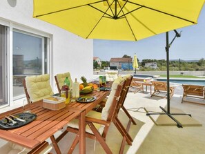 An outdoor patio with a wooden table set for dining, surrounded by chairs, and a yellow umbrella providing shade. - Villa Silente with pool and sauna by Interhome (Debeljak)