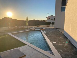 A swimming pool with a sunlit sky, a few lounge chairs, and a building in the background. - Villa Silente with pool and sauna by Interhome (Debeljak)