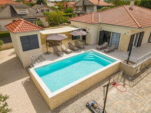 A swimming pool with lounge chairs and umbrellas, surrounded by a residential area. - Villa Paloma with heated pool by Interhome (Debeljak)