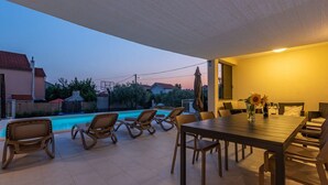 Patio esterno con piscina, sedie a sdraio e tavolo da pranzo con sedie.