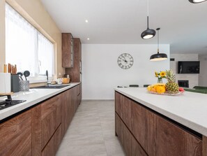 A modern kitchen with wooden cabinets, a central island with fruit, and a wall clock. - Villa Paloma with heated pool by Interhome (Debeljak)