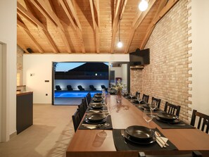 A dining area with a long wooden table set for a meal, a brick wall, and a view of an outdoor swimming pool. - Villa Marta with heated pool and traditional taver by Interhome (Debeljak)