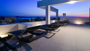 Ein Außenbereich mit Lounge-Möbeln und Tischen, einer Pergola und Blick auf die Landschaft.