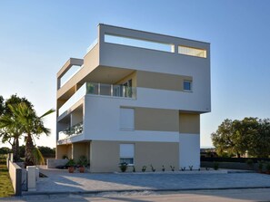Ein modernes, mehrgeschossiges Gebäude mit Balkonen, einer flachen Dachterrasse und blauem Himmel.