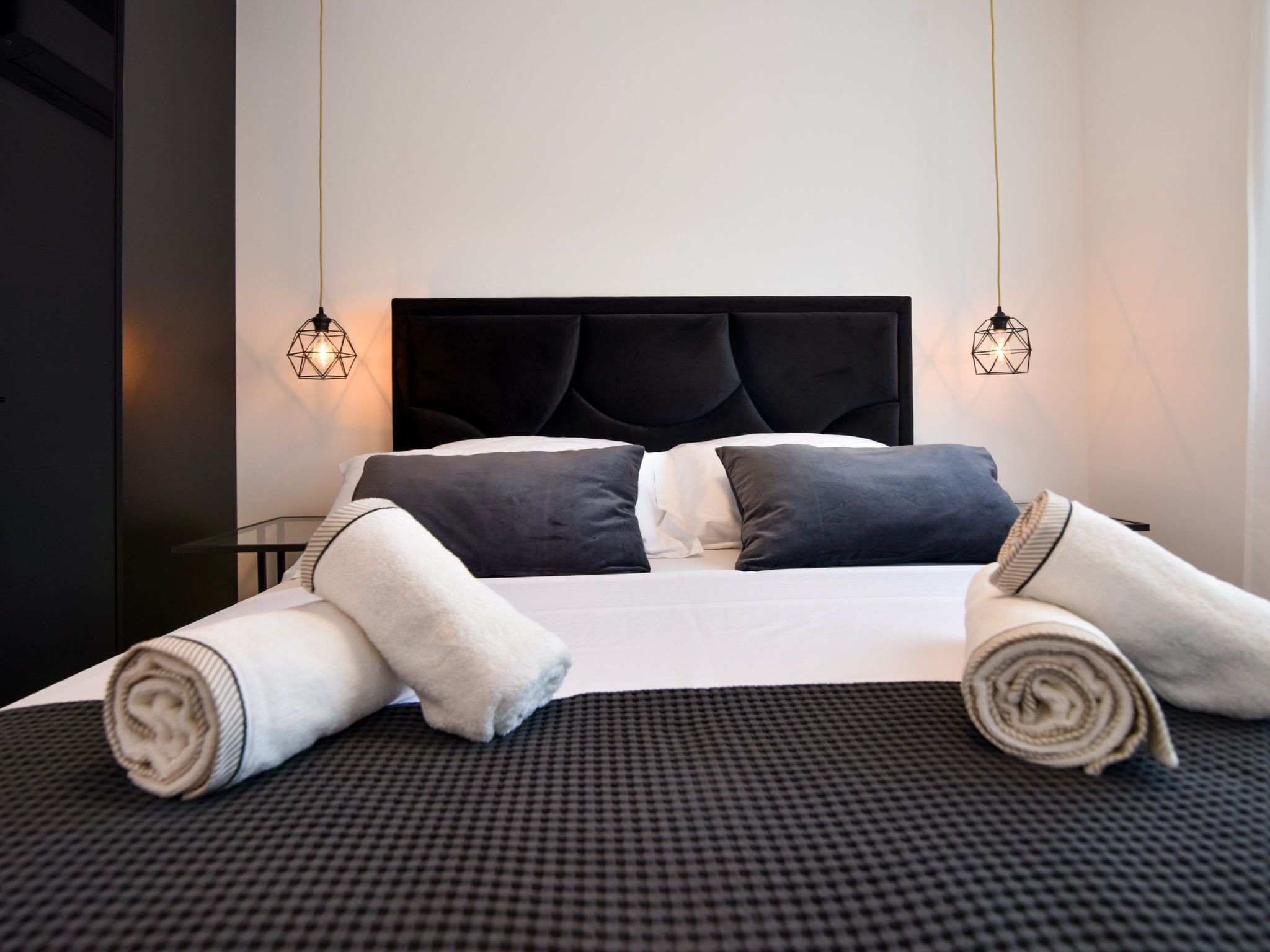A neatly made bed with a black headboard, two bedside lamps, and rolled towels on the bed.