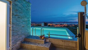 An outdoor swimming pool with a stone wall and a view of a cityscape at dusk. - Vacation home  by Interhome (Crno)