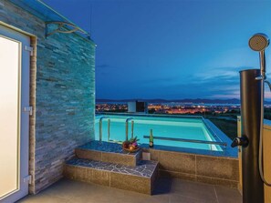 Ein Pool im Freien mit einer Steinmauer und Blick auf eine städtische Skyline in der Dämmerung.