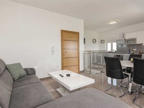 Ein modernes Wohnzimmer mit einem grauen Sofa, einem weißen Couchtisch und einem Essbereich mit schwarzen Stühlen.