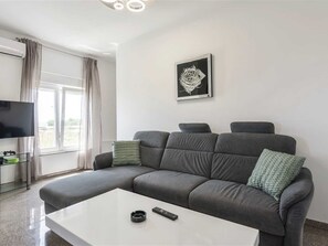 A modern living room with a grey sofa, a white coffee table, a remote control, and a framed artwork on the wall.